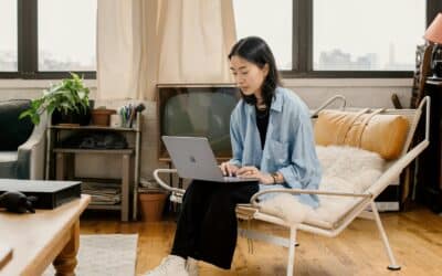 woman in blue shirt sitting on white chair using Surface laptop