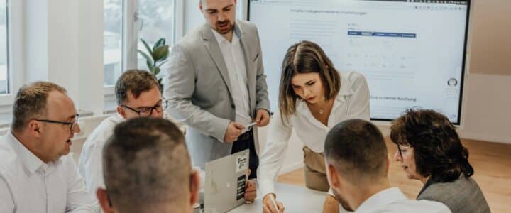 a group of people sitting around a table with laptops