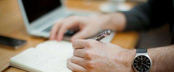 man sitting while writing on notebook